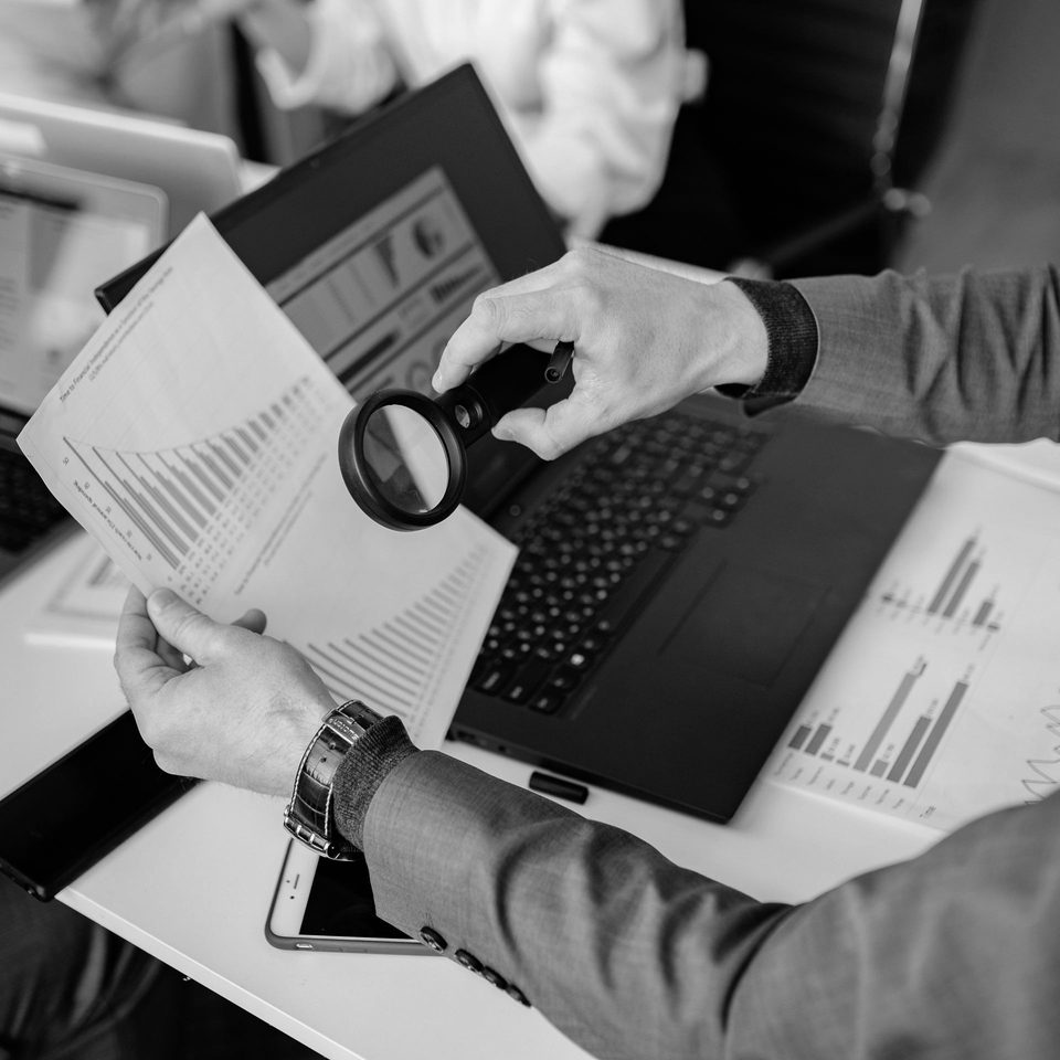 A person closely examining a business analytics report with a magnifying glass
